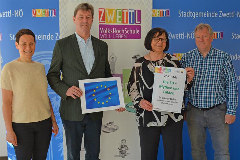 Vier Personen vor einer blauen Fotowand, in der Hand mit Foto einer EU-Fahne